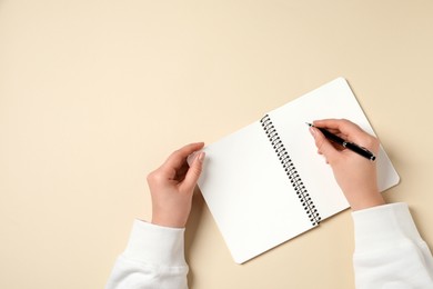 Photo of Woman with pen and notepad on beige background, top view. Space for text