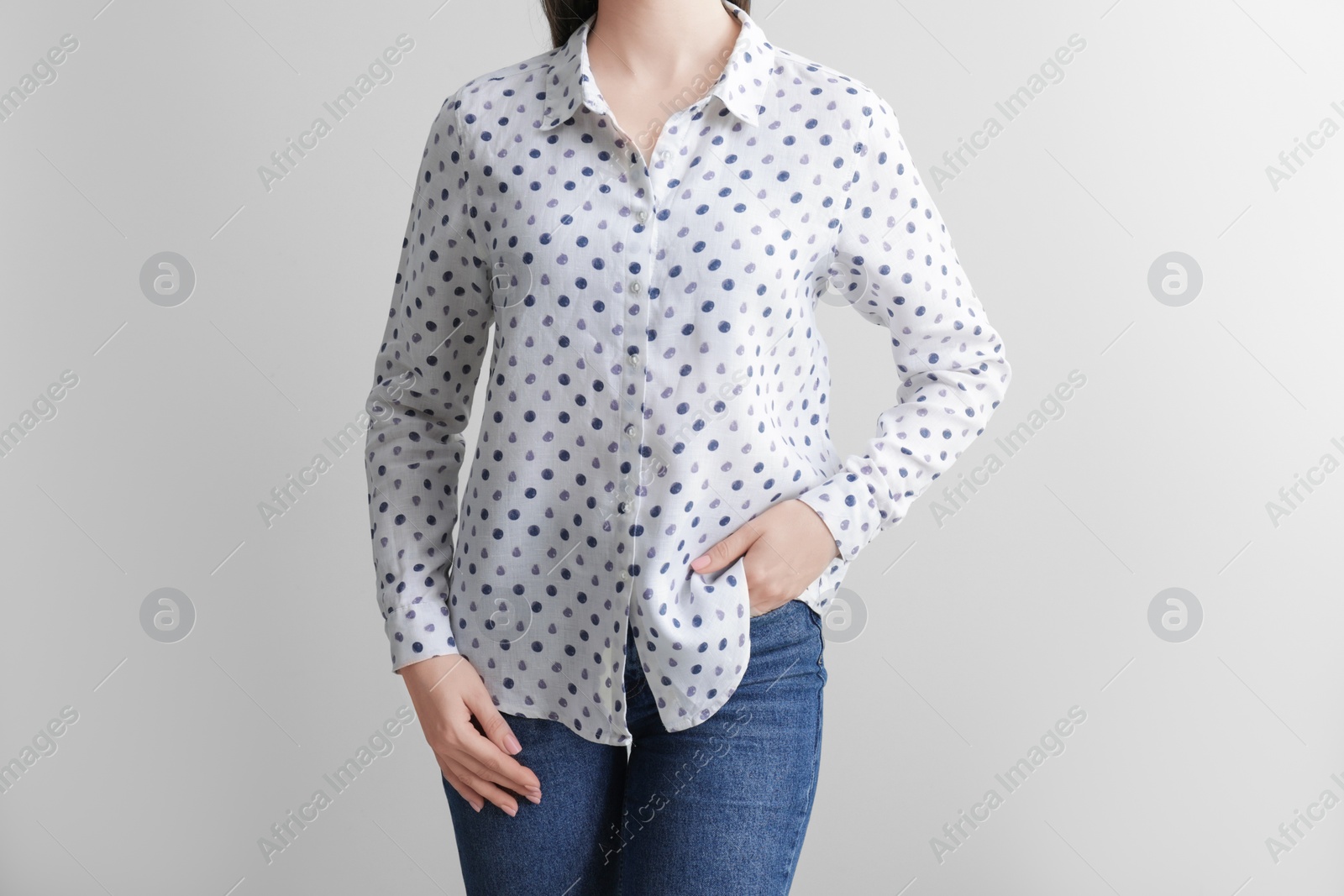 Photo of Woman wearing wrinkled white polka dot blouse on light grey background, closeup