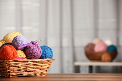 Photo of Wicker basket with clews of colorful knitting threads and crochet hooks on wooden table indoors. Space for text