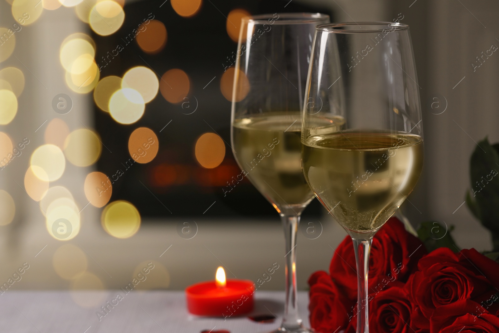 Photo of Glasses of white wine, burning candle and rose flowers on grey table indoors, space for text. Romantic atmosphere