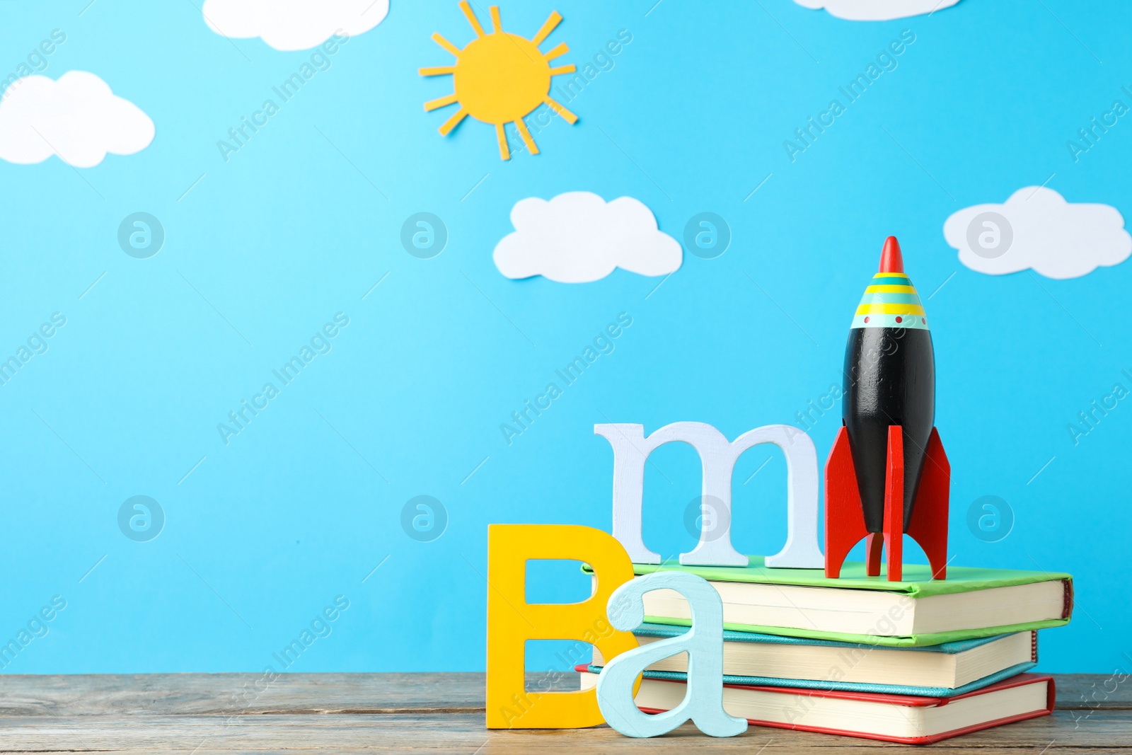 Photo of Bright toy rocket and school supplies on wooden table. Space for text