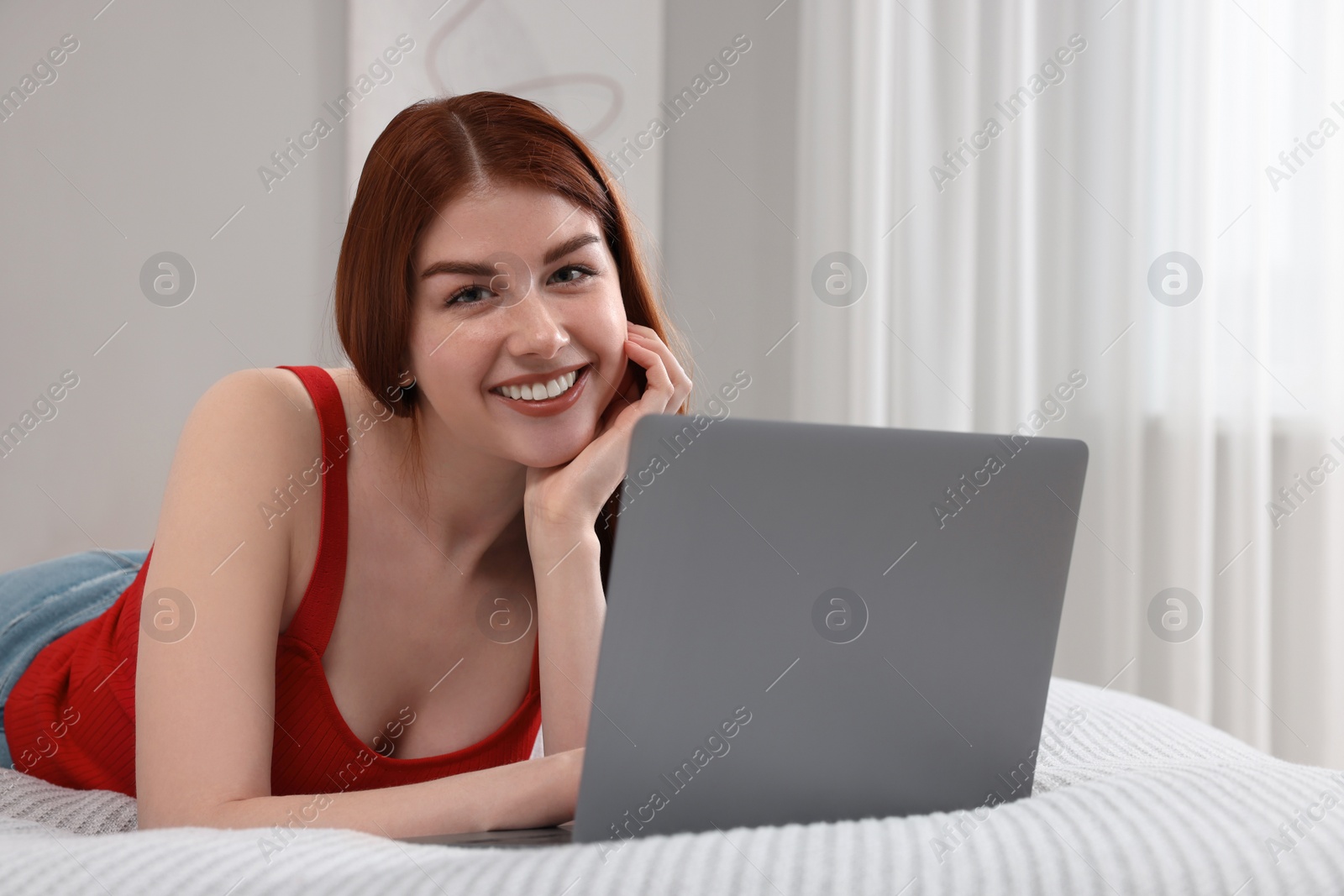 Photo of Happy woman with laptop on bed in bedroom