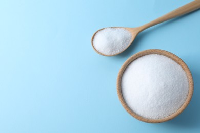 Photo of Organic white salt in bowl and spoon on light blue background, top view. Space for text