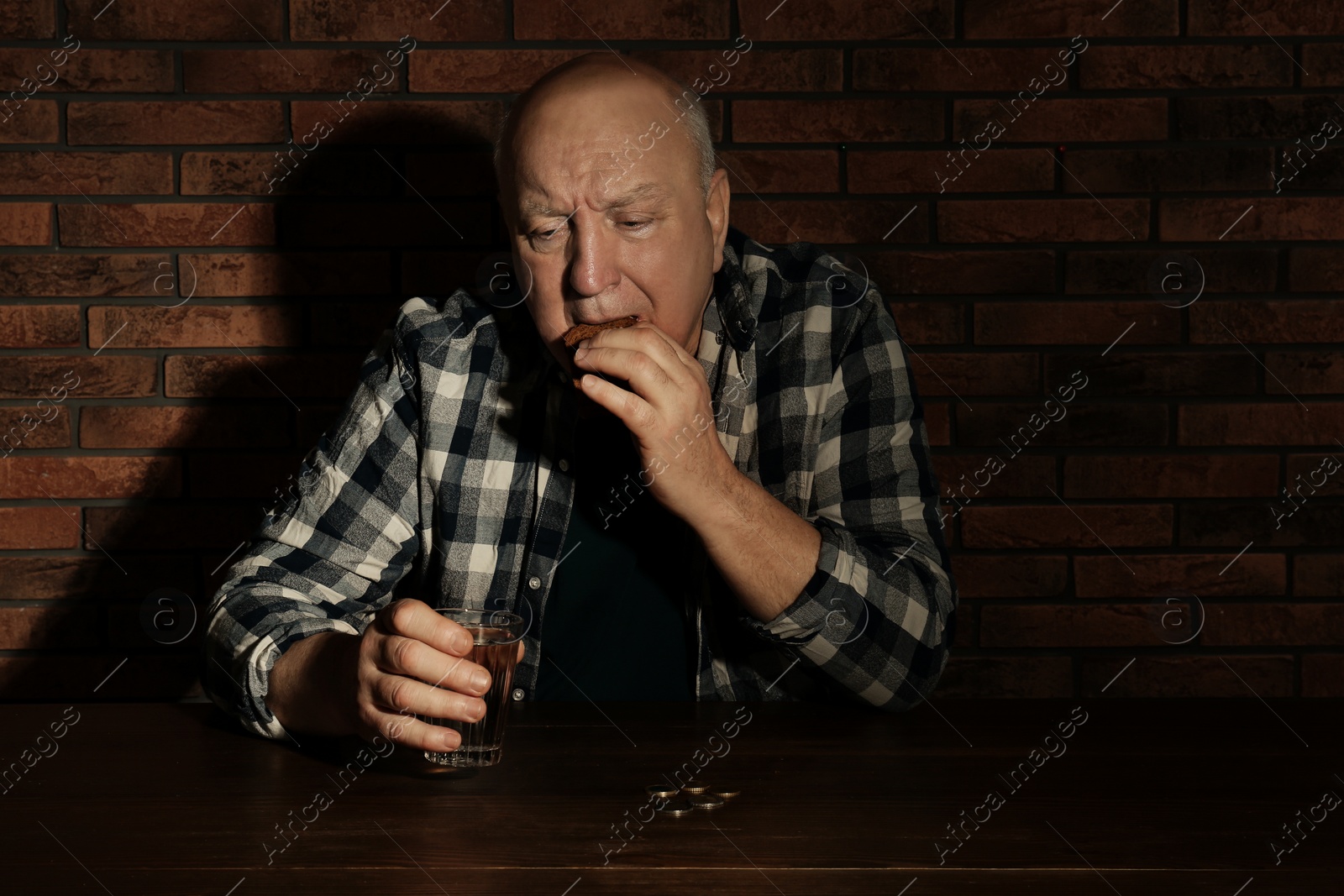 Photo of Poor senior man with bread and glass of water at table near brick wall