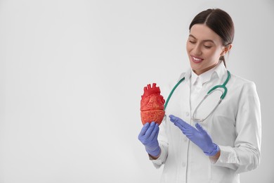 Doctor with stethoscope and model of heart on white background, space for text. Cardiology concept