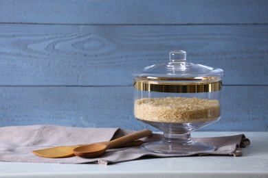 Photo of Raw rice on grey table against blue wooden background, space for text. Foodstuff for modern kitchen