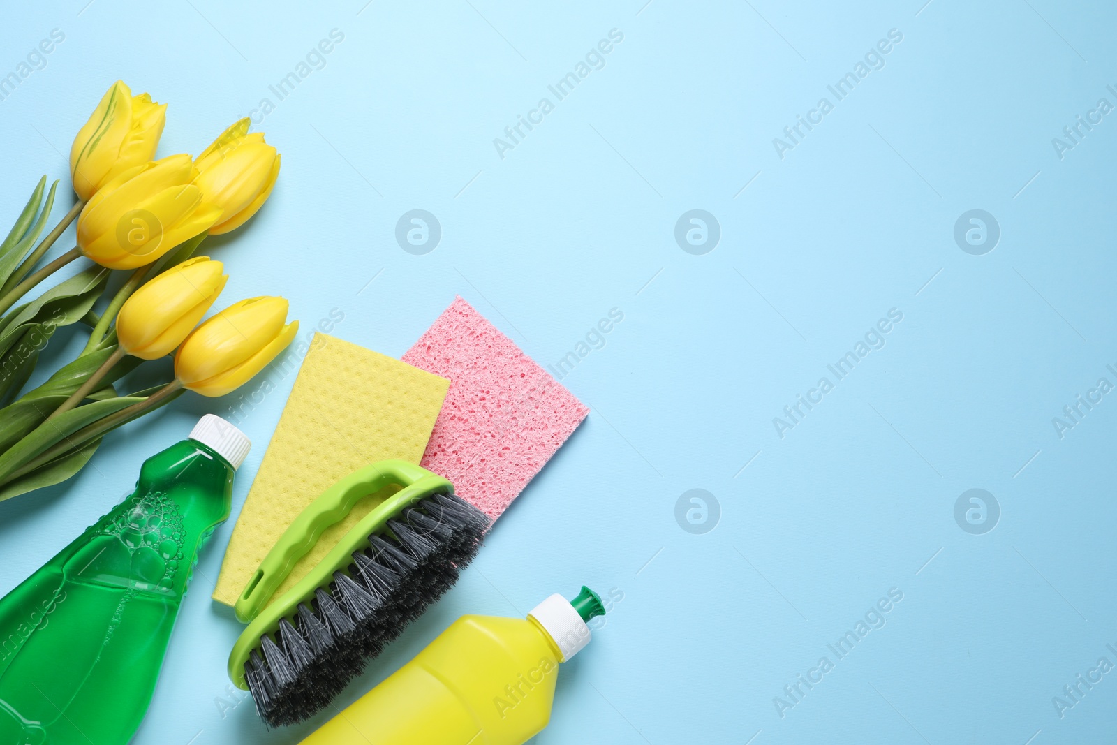 Photo of Spring cleaning. Detergents, flowers, brush and rags on light blue background, flat lay. Space for text