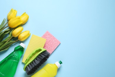 Spring cleaning. Detergents, flowers, brush and rags on light blue background, flat lay. Space for text