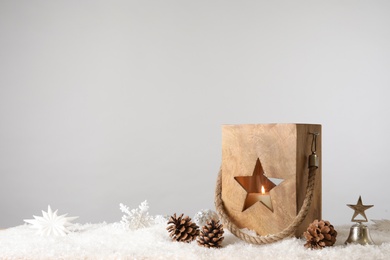 Composition with wooden Christmas lantern on snow against light grey background, space for text