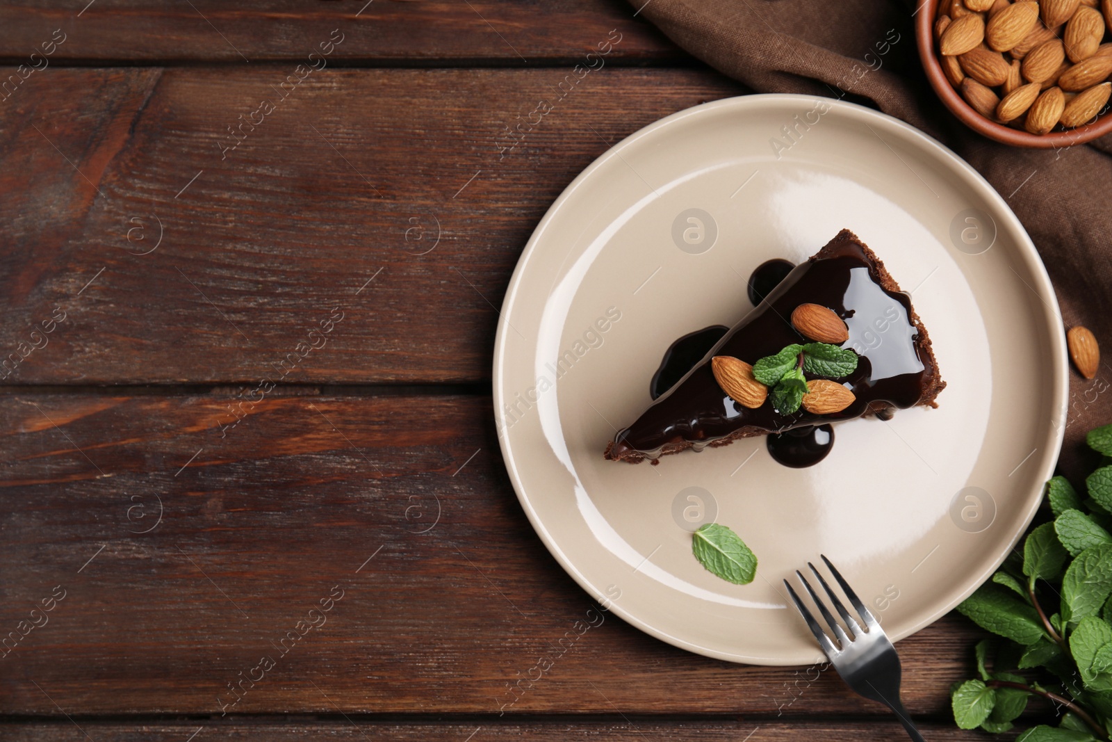 Photo of Piece of tasty homemade chocolate cake with mint and almonds on wooden table, flat lay. Space for text