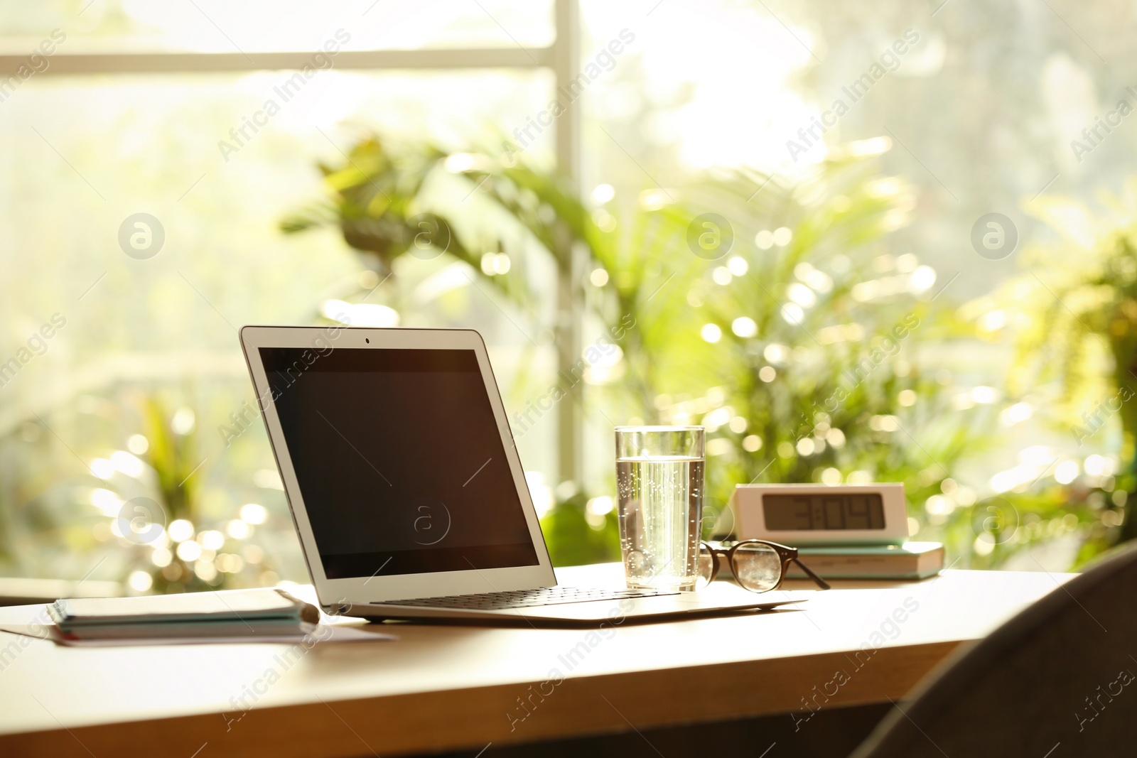 Photo of Modern laptop and glass of water on table in office