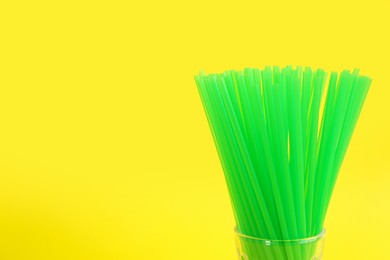 Green plastic drinking straws in glass on yellow background, closeup. Space for text