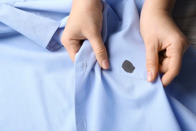 Photo of Woman holding shirt with black ink stain, top view