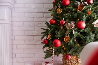 Photo of Beautiful decorated Christmas tree near white brick wall indoors, closeup. Space for text