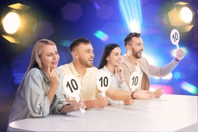 Panel of judges holding signs with highest score at table against blurred background