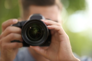 Photo of Photographer taking picture with professional camera outdoors, focus on lens
