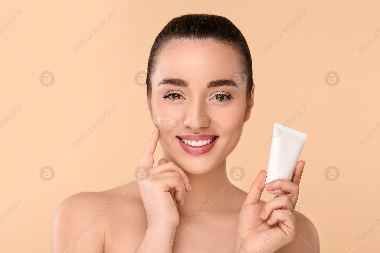 Photo of Woman holding tube of foundation on beige background