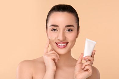 Photo of Woman holding tube of foundation on beige background