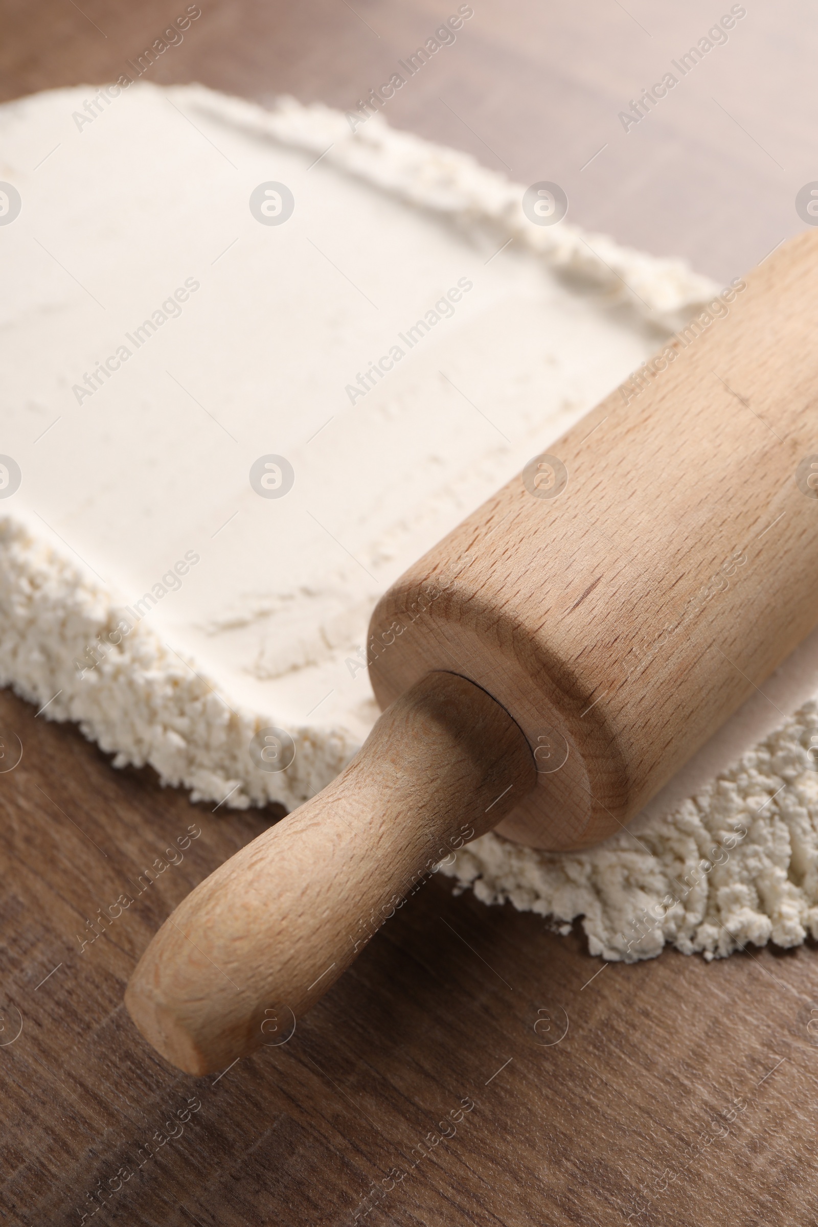 Photo of Flour and rolling pin on wooden table, closeup