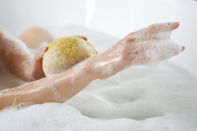 Photo of Woman rubbing her forearm with sponge while taking bath, closeup