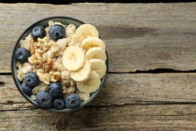 Photo of Tasty oatmeal with banana, blueberries and walnuts served in bowl on wooden table, top view. Space for text