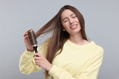 Photo of Upset woman brushing her hair on grey background. Alopecia problem