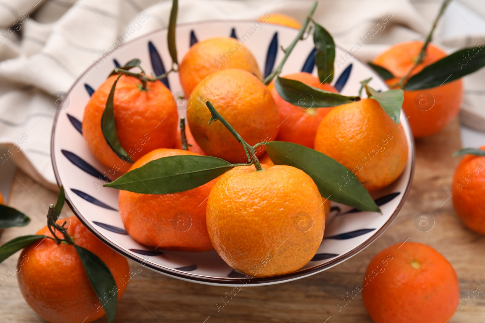 Photo of Fresh ripe tangerines with green leaves in bowl on wooden table, closeup