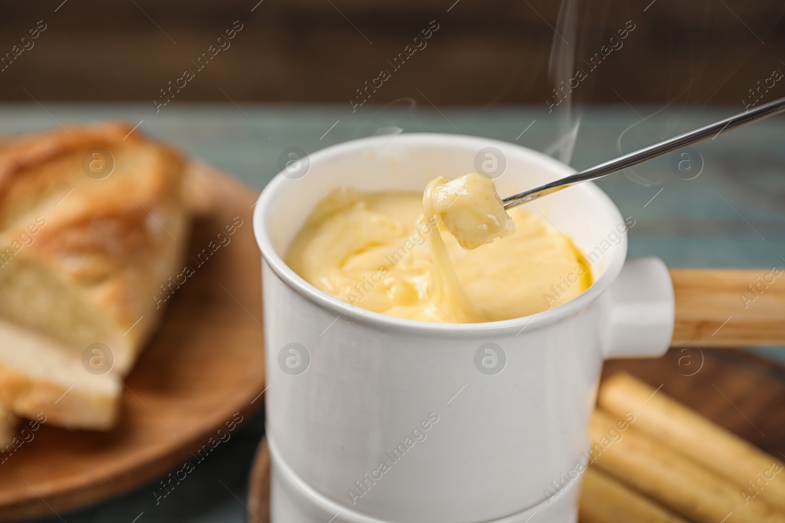 Photo of Pot of tasty cheese fondue and fork with bread on blue wooden table