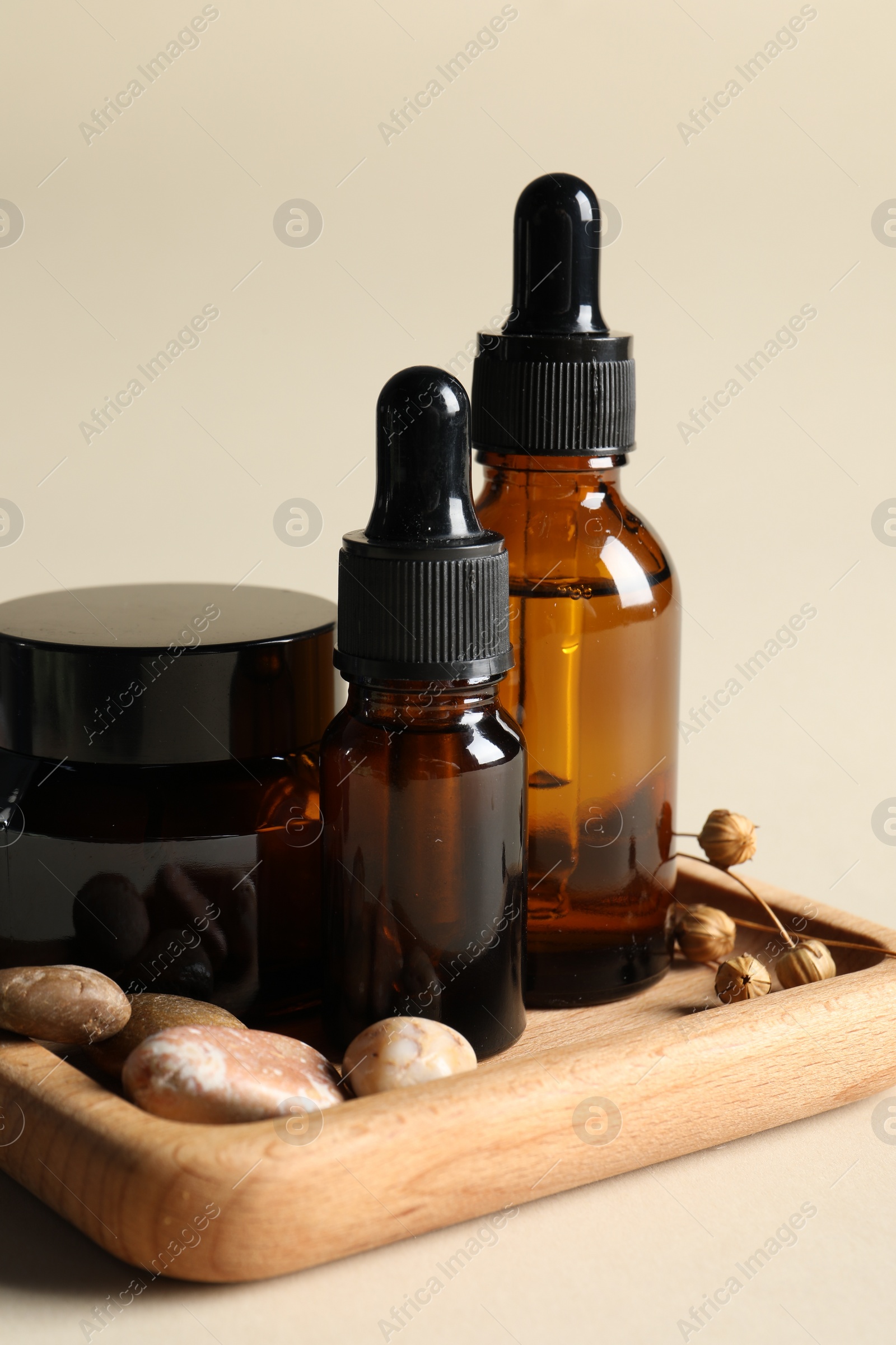 Photo of Wooden tray with bottles of cosmetic serum, jar and stones on beige background, closeup