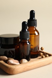 Photo of Wooden tray with bottlescosmetic serum, jar and stones on beige background, closeup