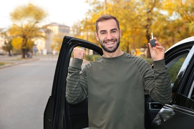 Young man holding car key near auto. Driving license test