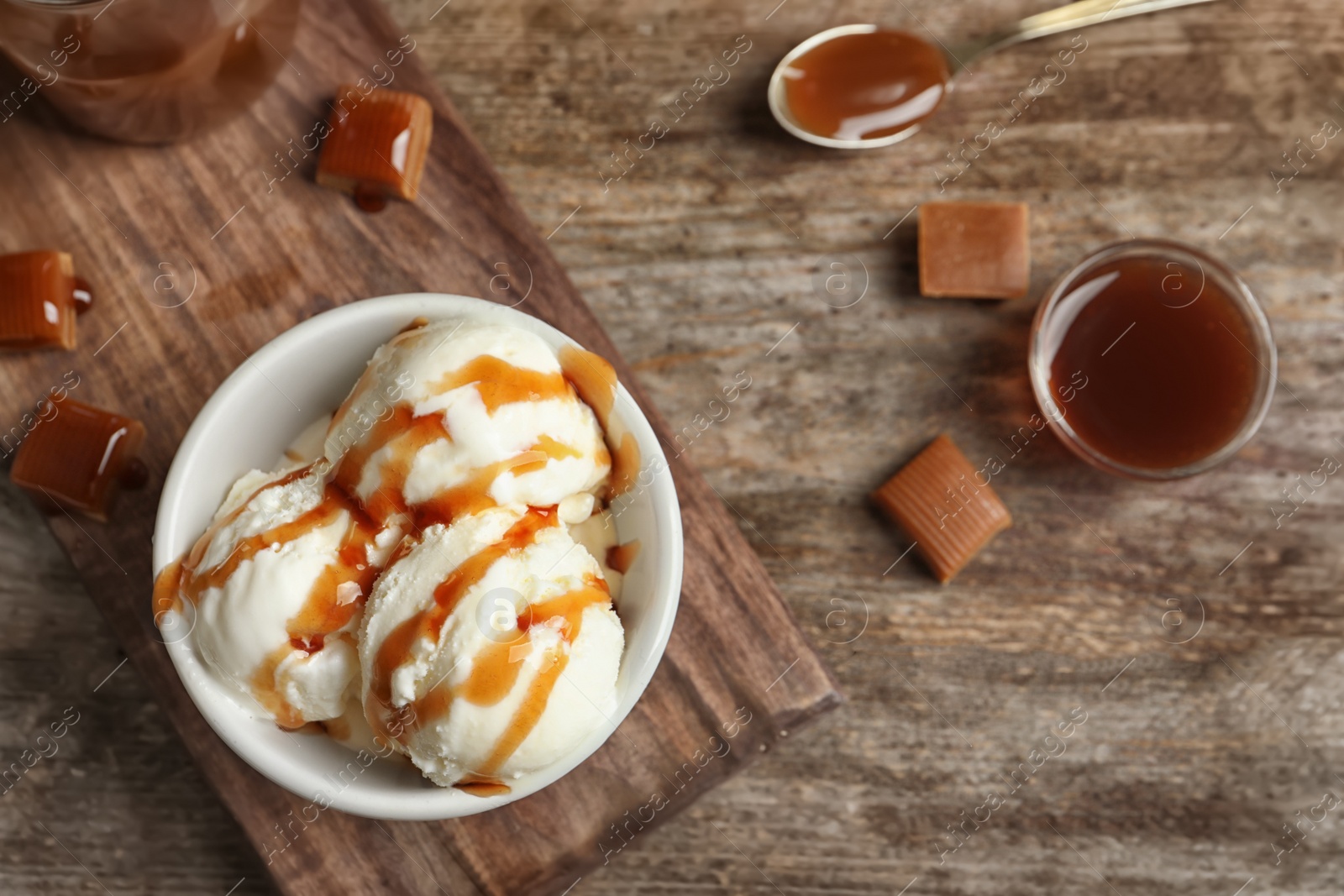 Photo of Tasty ice cream with caramel sauce in bowl on wooden board