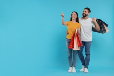 Happy couple with shopping bags looking at something on light blue background. Space for text