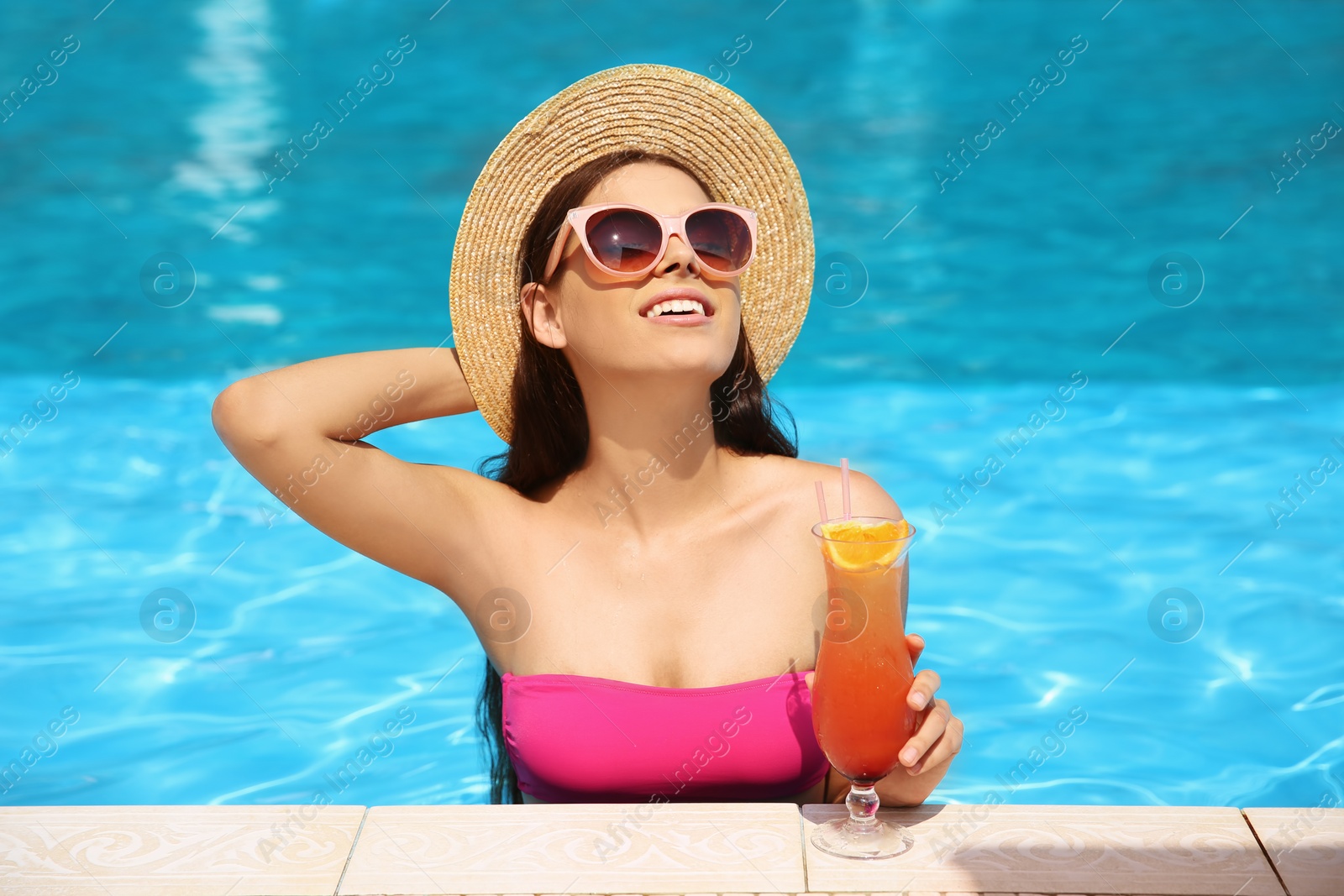 Photo of Beautiful young woman with cocktail in blue swimming pool