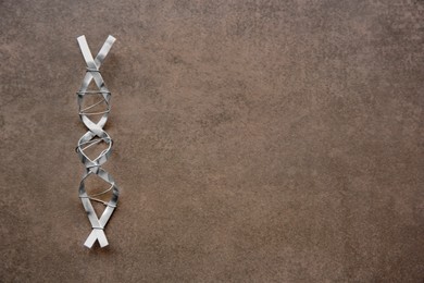Photo of DNA molecule model made of metal on brown background, top view. Space for text