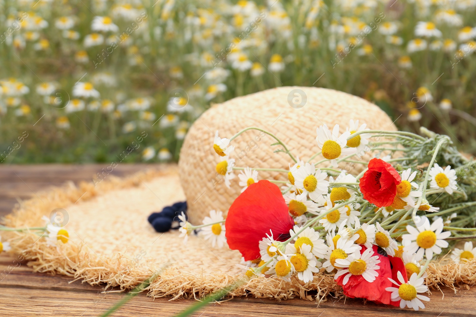 Photo of Bouquet of poppies and chamomiles with straw hat on wooden table outdoors