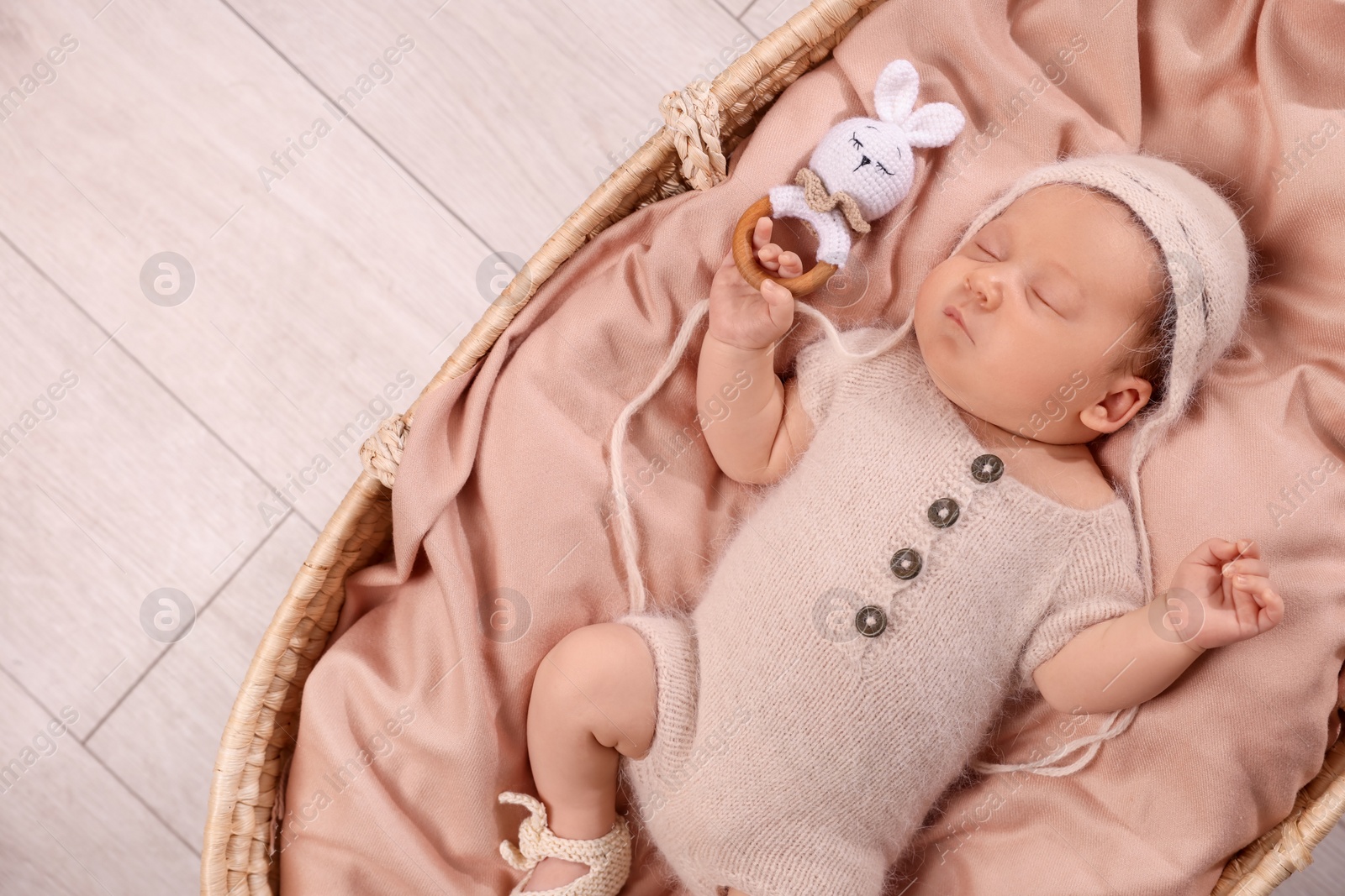 Photo of Cute newborn baby sleeping with rattle in wicker crib indoors, top view. Space for text