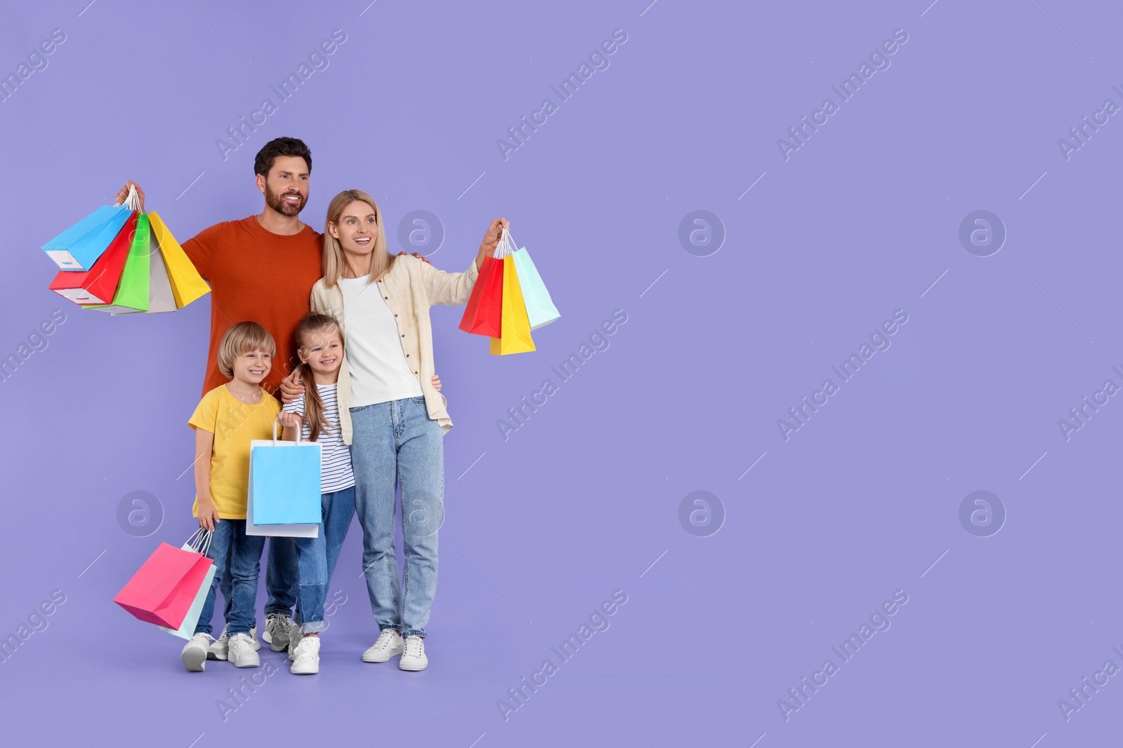 Photo of Family shopping. Happy parents and children with many colorful bags on violet background. Space for text