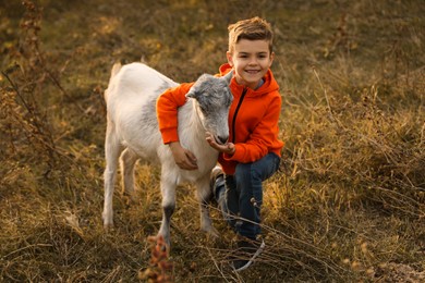 Photo of Farm animal. Cute little boy feeding goat on pasture