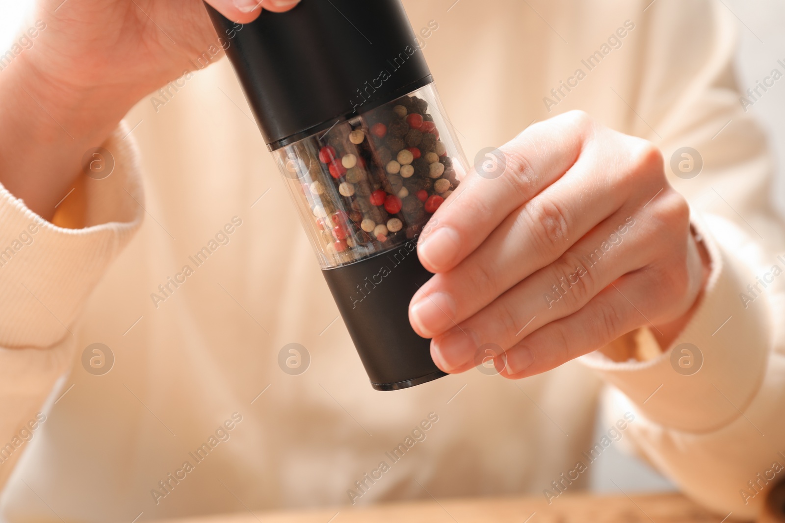 Photo of Woman grinding pepper with shaker at table, closeup