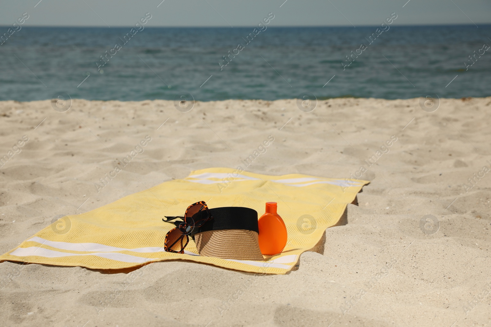 Photo of Beach towel with visor cap, sunglasses and sunscreen on sand near sea