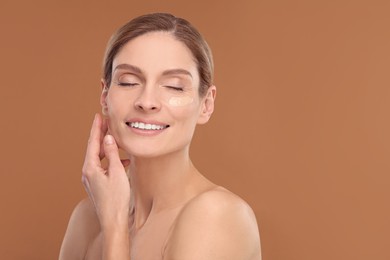 Woman with swatch of foundation on face against brown background. Space for text