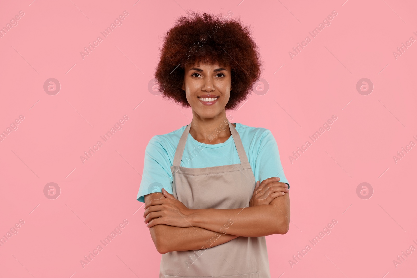 Photo of Portrait of happy young woman in apron on pink background