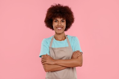 Photo of Portrait of happy young woman in apron on pink background