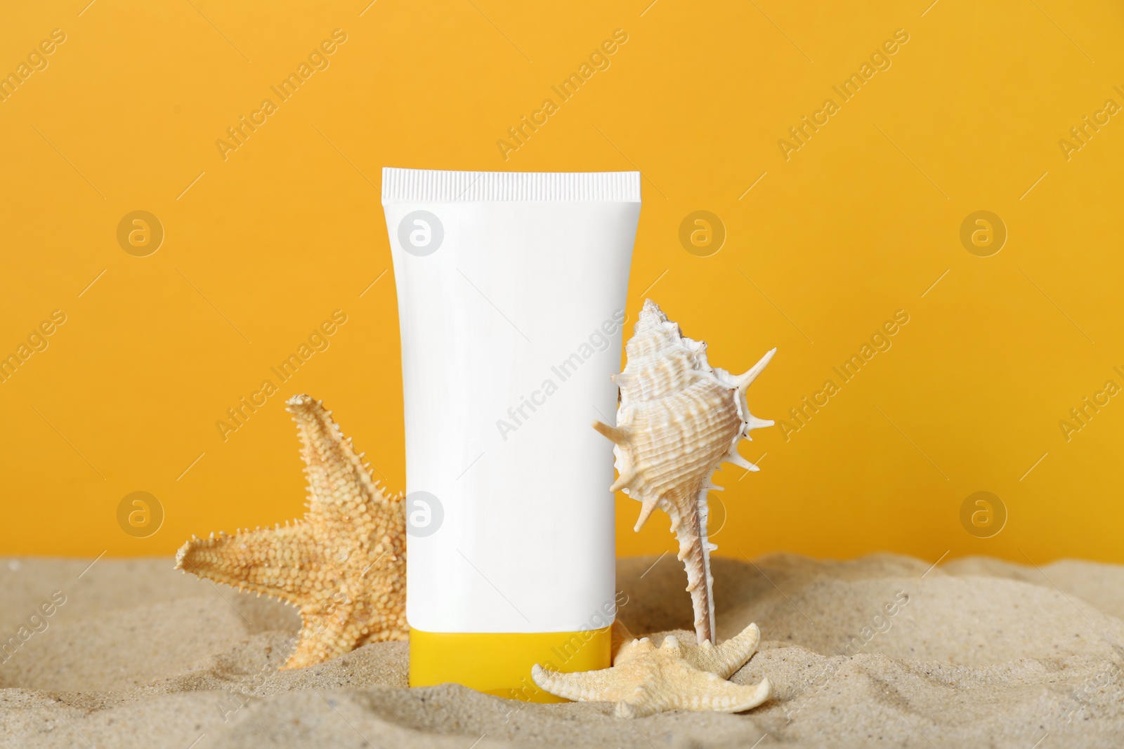 Photo of Suntan product, seashell and starfishes on sand against yellow background
