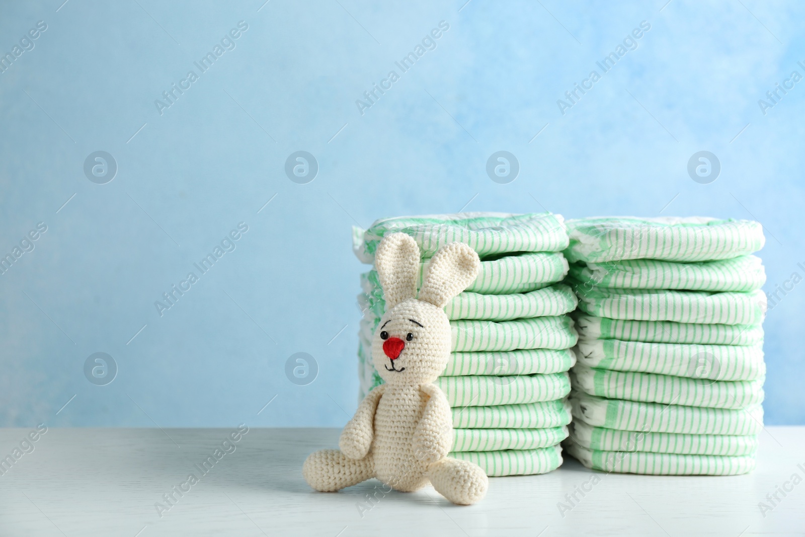 Photo of Stacks of diapers and toy bunny on table against color background, space for text. Baby accessories