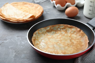 Photo of Delicious thin pancake in frying pan on grey table, closeup