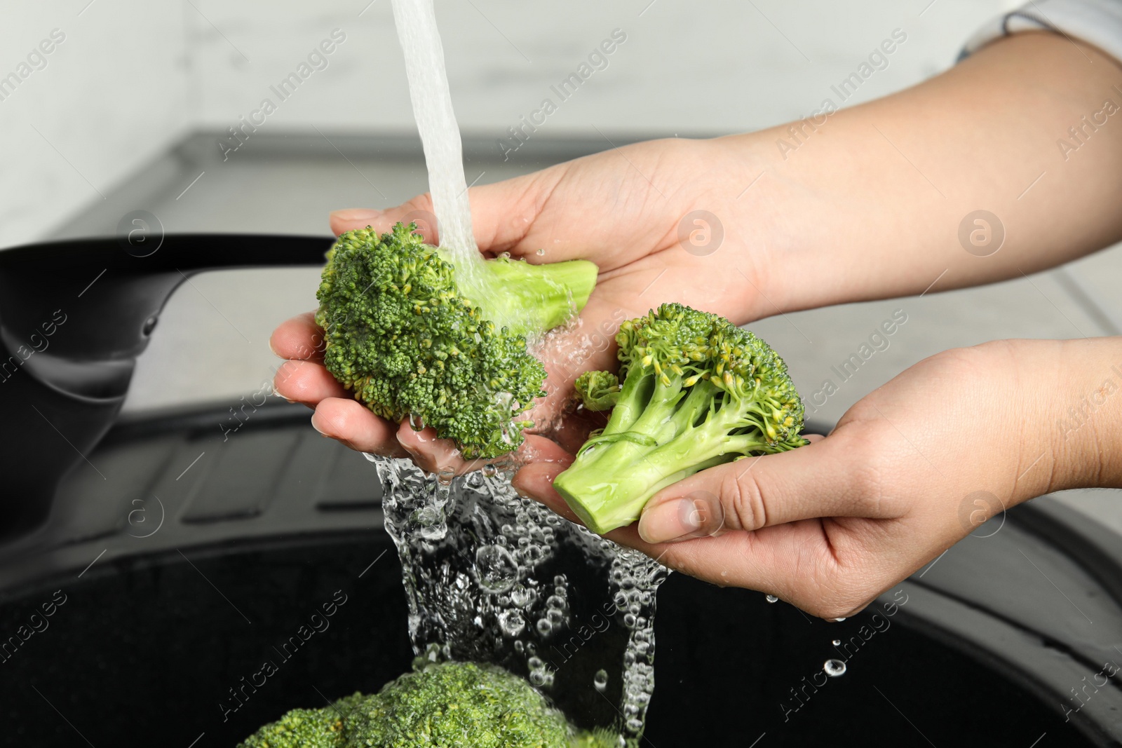 Photo of Woman washing fresh green broccoli in kitchen sink, closeup