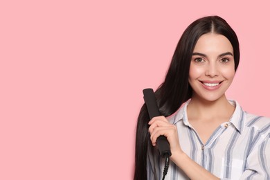Beautiful happy woman using hair iron on pink background. Space for text