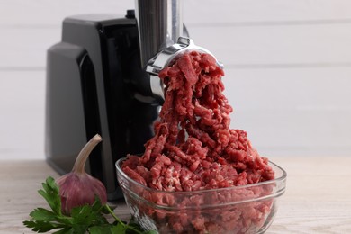 Photo of Electric meat grinder with beef mince, garlic and parsley on white wooden table